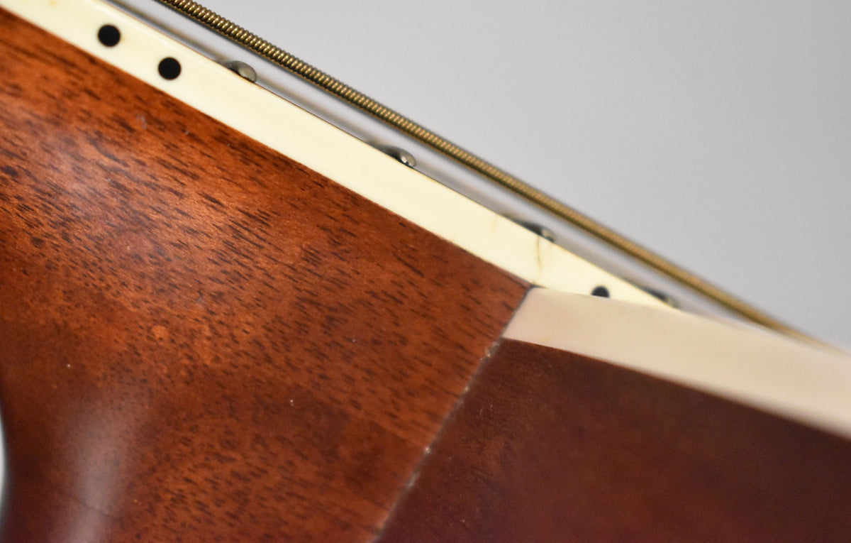 Close-up of the guitar's mahogany neck and body joint, showing cream binding and a few small dents on the neck.