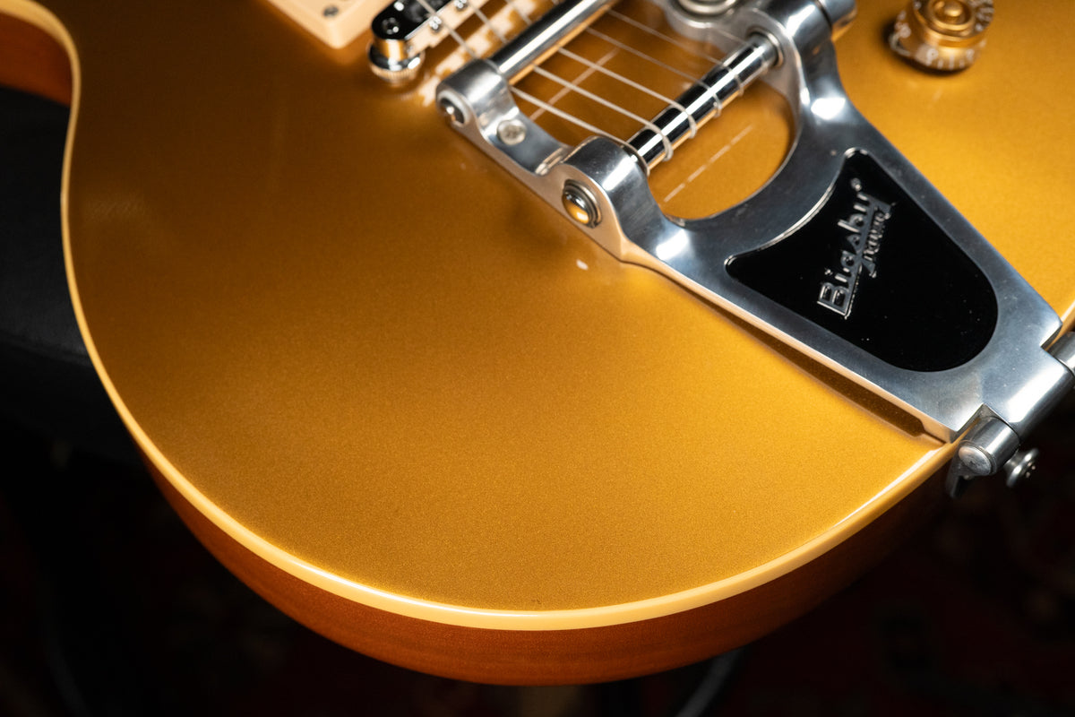 Close-up of the guitar's lower bout, showing the metallic goldtop finish, cream binding, and a chrome Bigsby vibrato system.