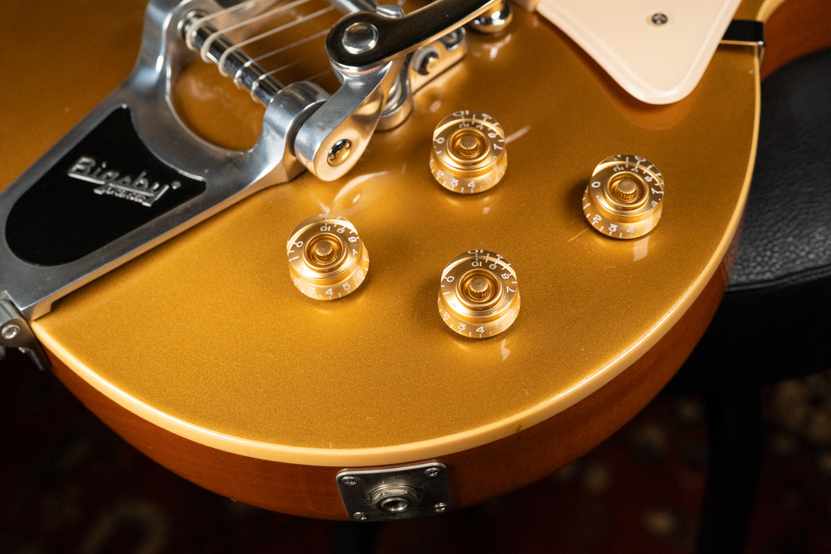 Close-up of the goldtop body, showing four gold bell knobs with clear tops, a Bigsby vibrato, and the input jack.