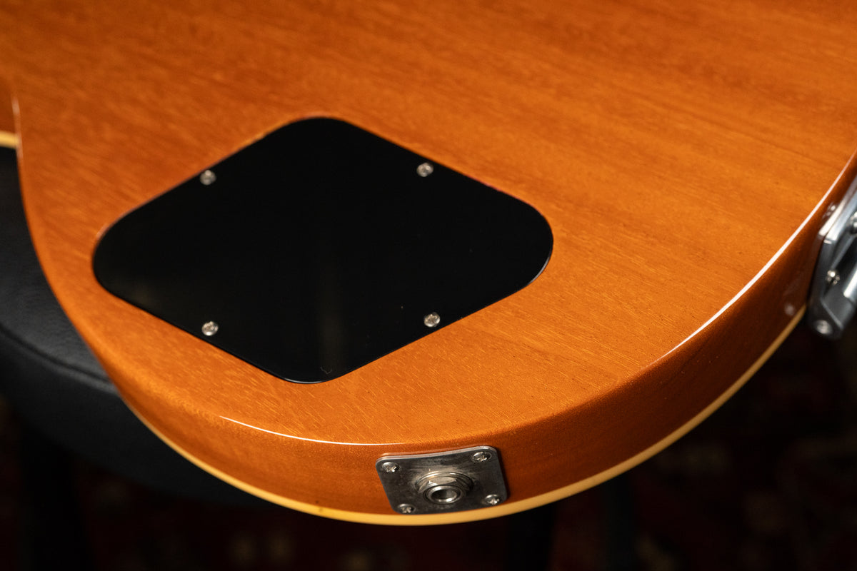 Close-up of the guitar's lower back, showing the amber-finished body, black control cavity cover, and chrome output jack plate.