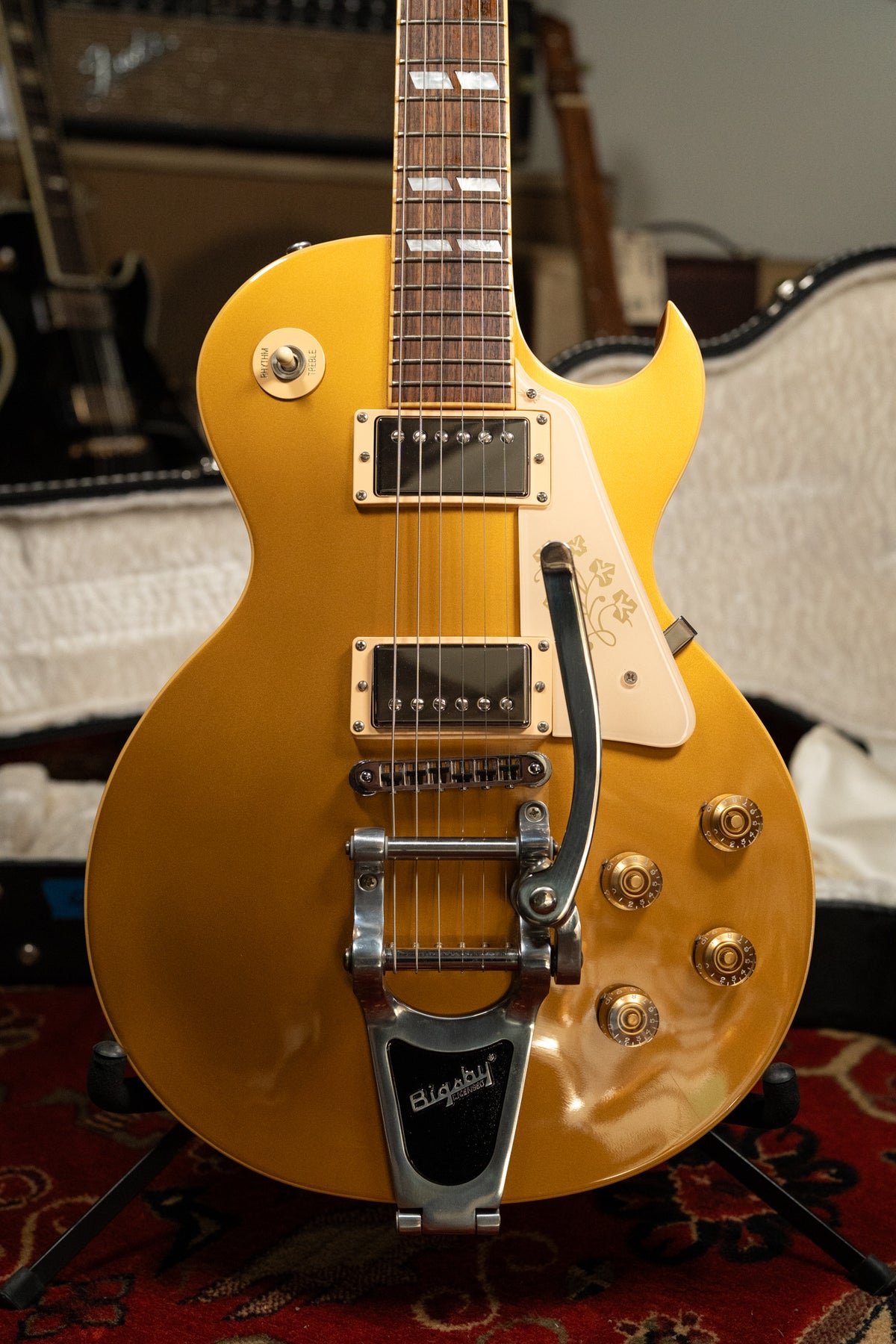 A goldtop Les Paul with a Bigsby vibrato, cream pickguard with floral etching, and four gold control knobs.