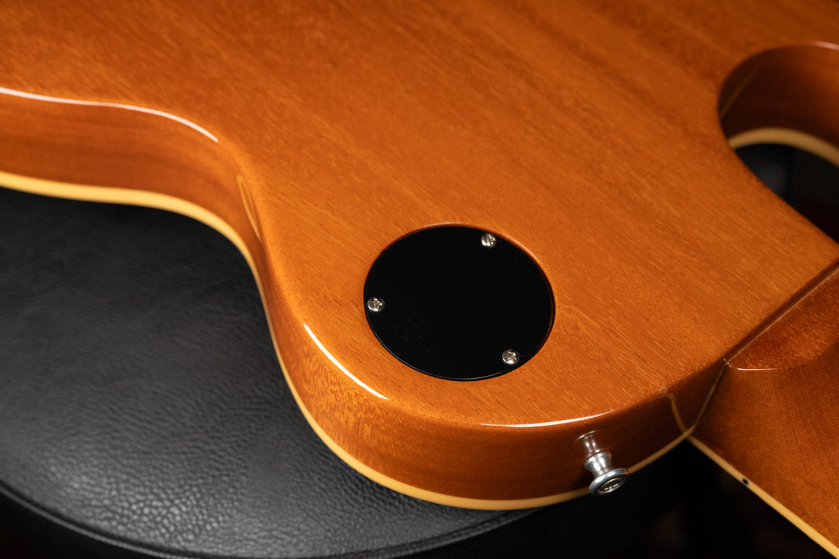 Close-up of the guitar's lower back, showing the glossy amber finish, cream binding, black control cavity cover, and strap button.