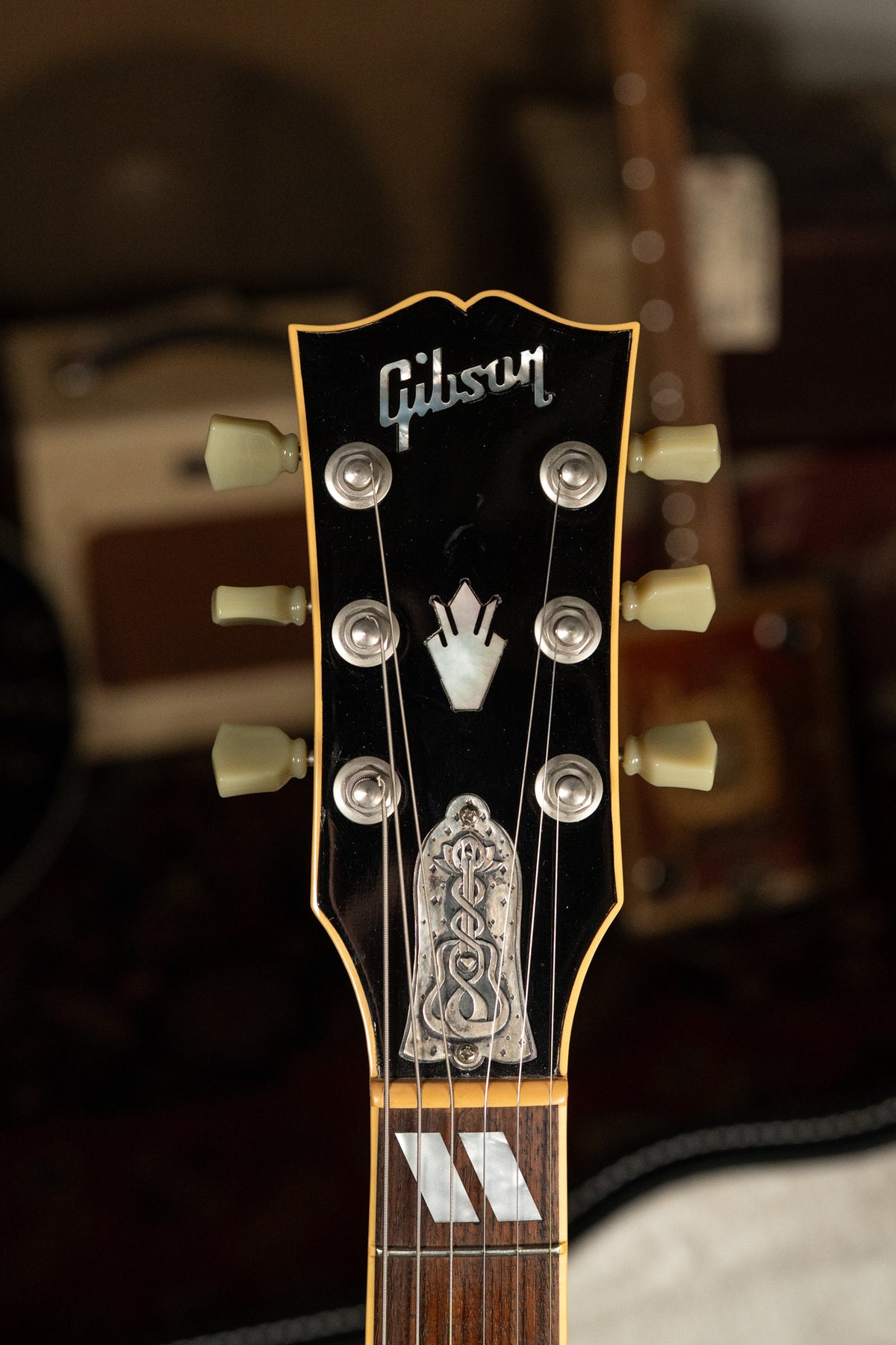 Close-up of the black headstock with cream binding, showing six cream tuners, mother-of-pearl inlays, and an engraved truss rod cover.