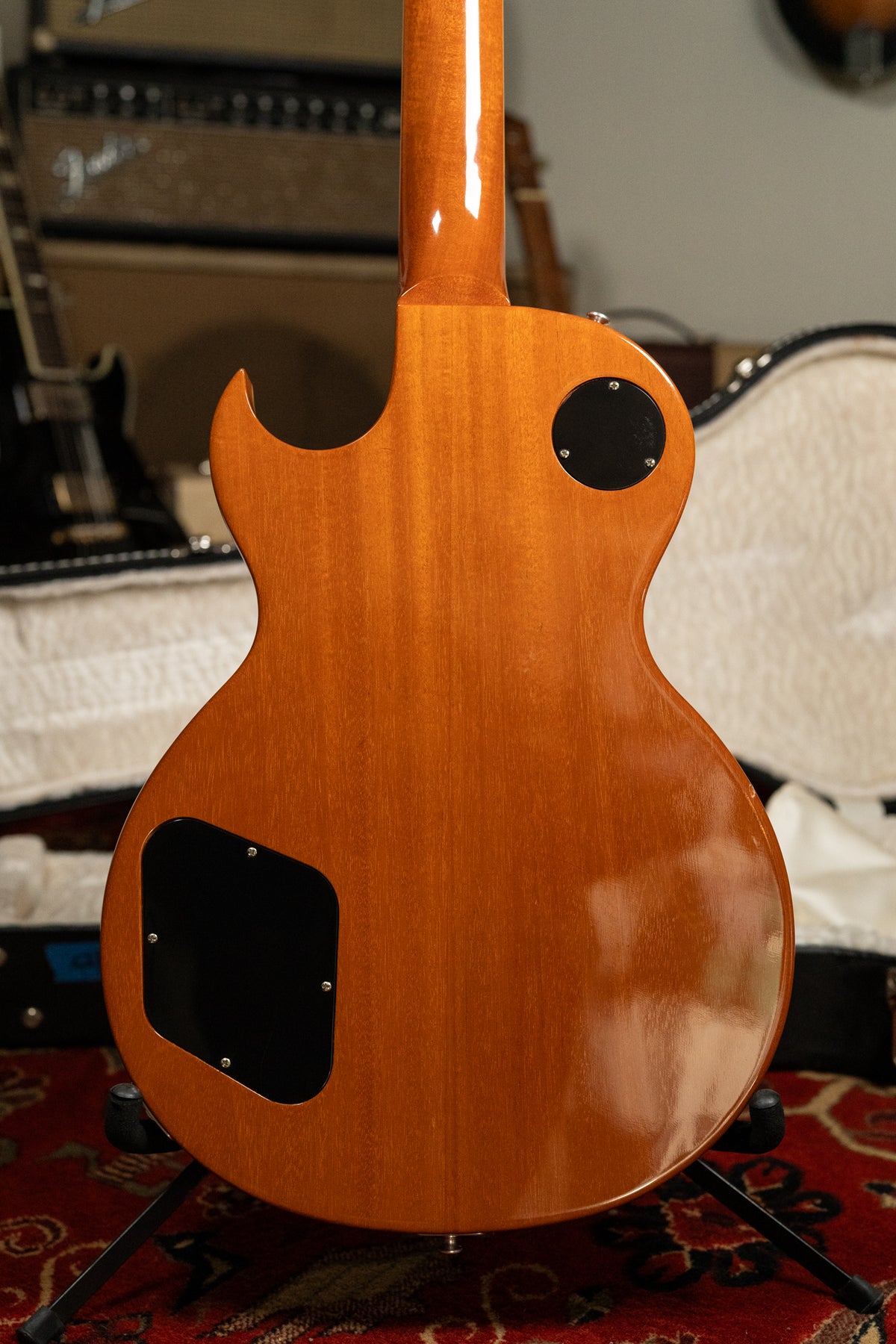 The back of the guitar shows a glossy, warm brown finish with visible wood grain, two black control cavity covers, and a slight ding on the lower bout.