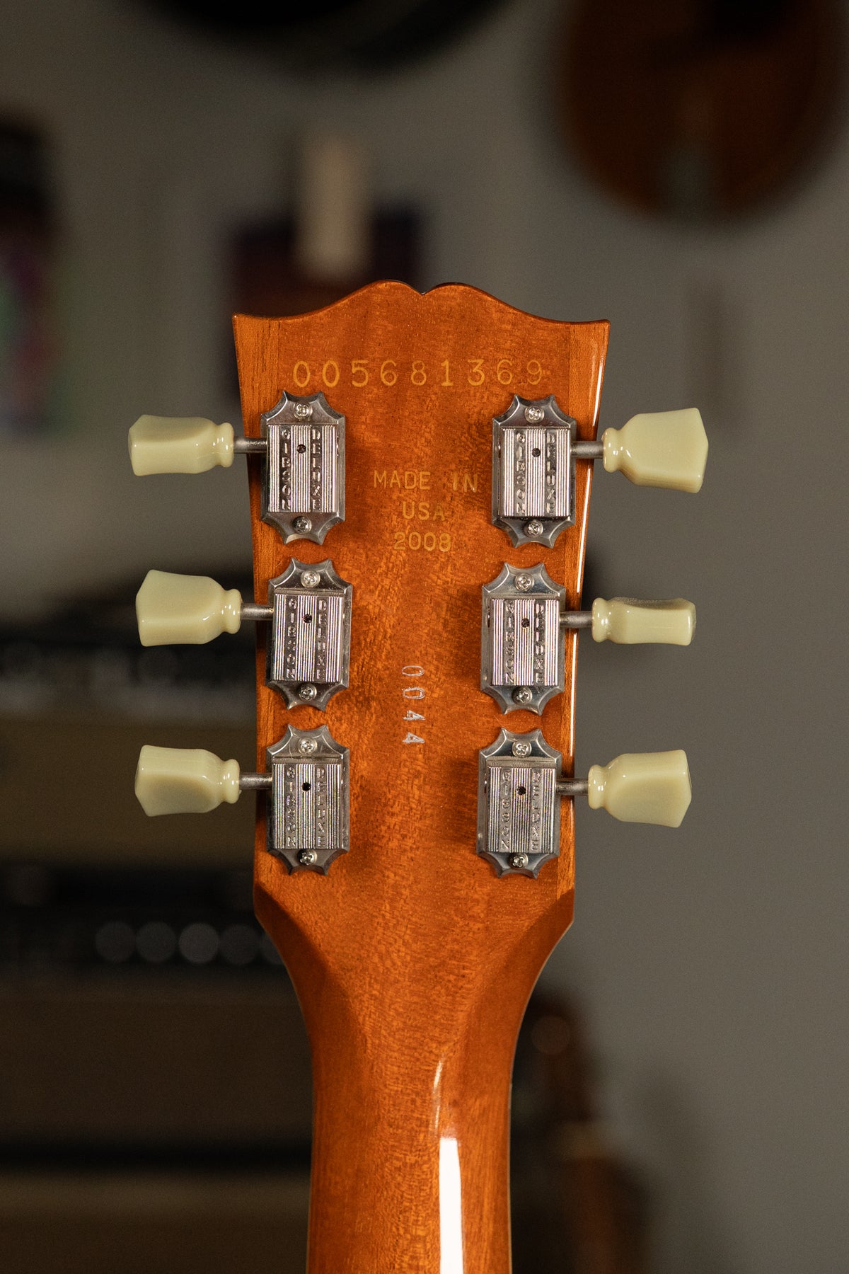 The back of a glossy amber headstock with six cream tuning pegs and ornate silver tuners, showing light wear.
