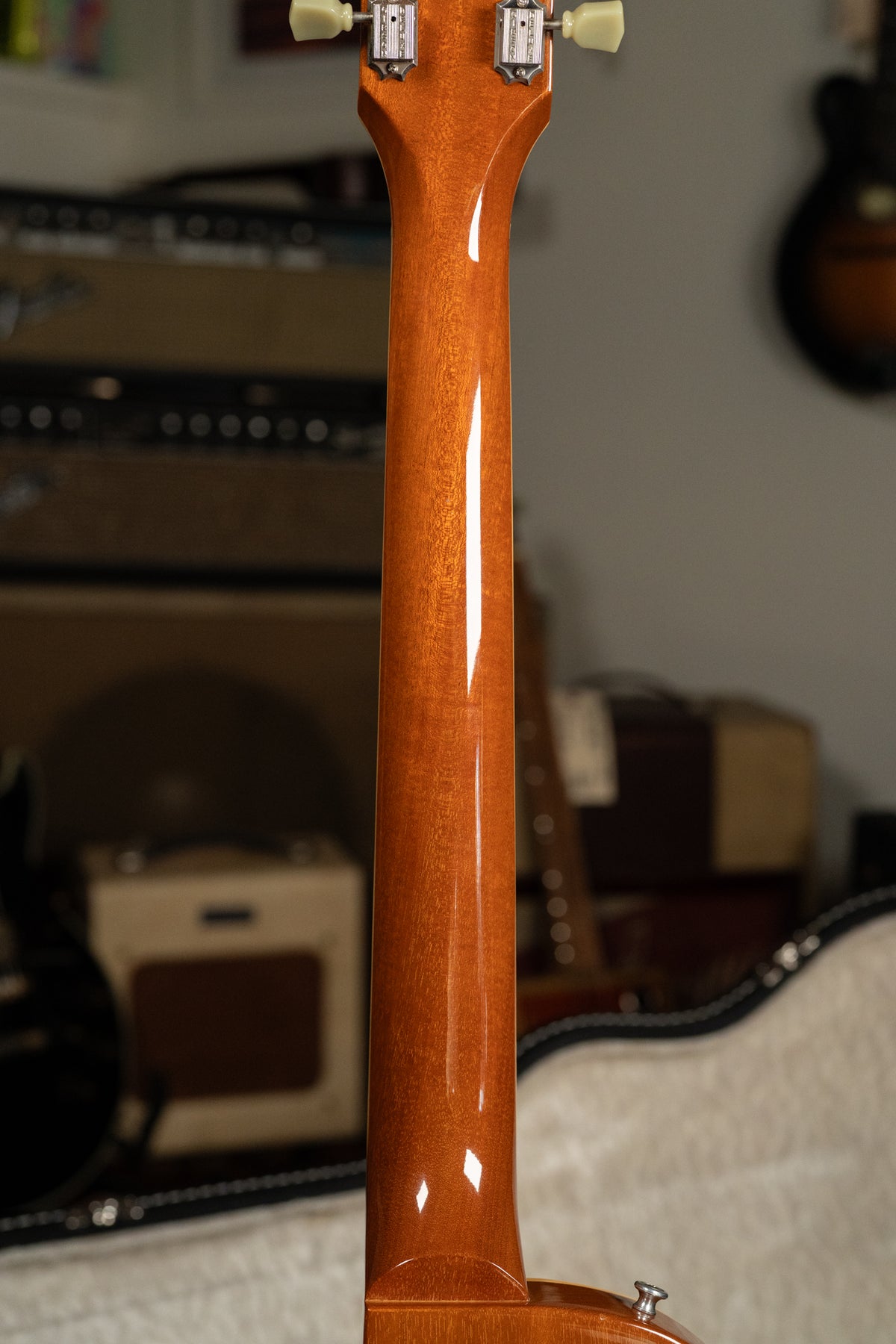 The back of the guitar's glossy, amber-stained neck and headstock, with cream tuning pegs and chrome tuners, is shown.