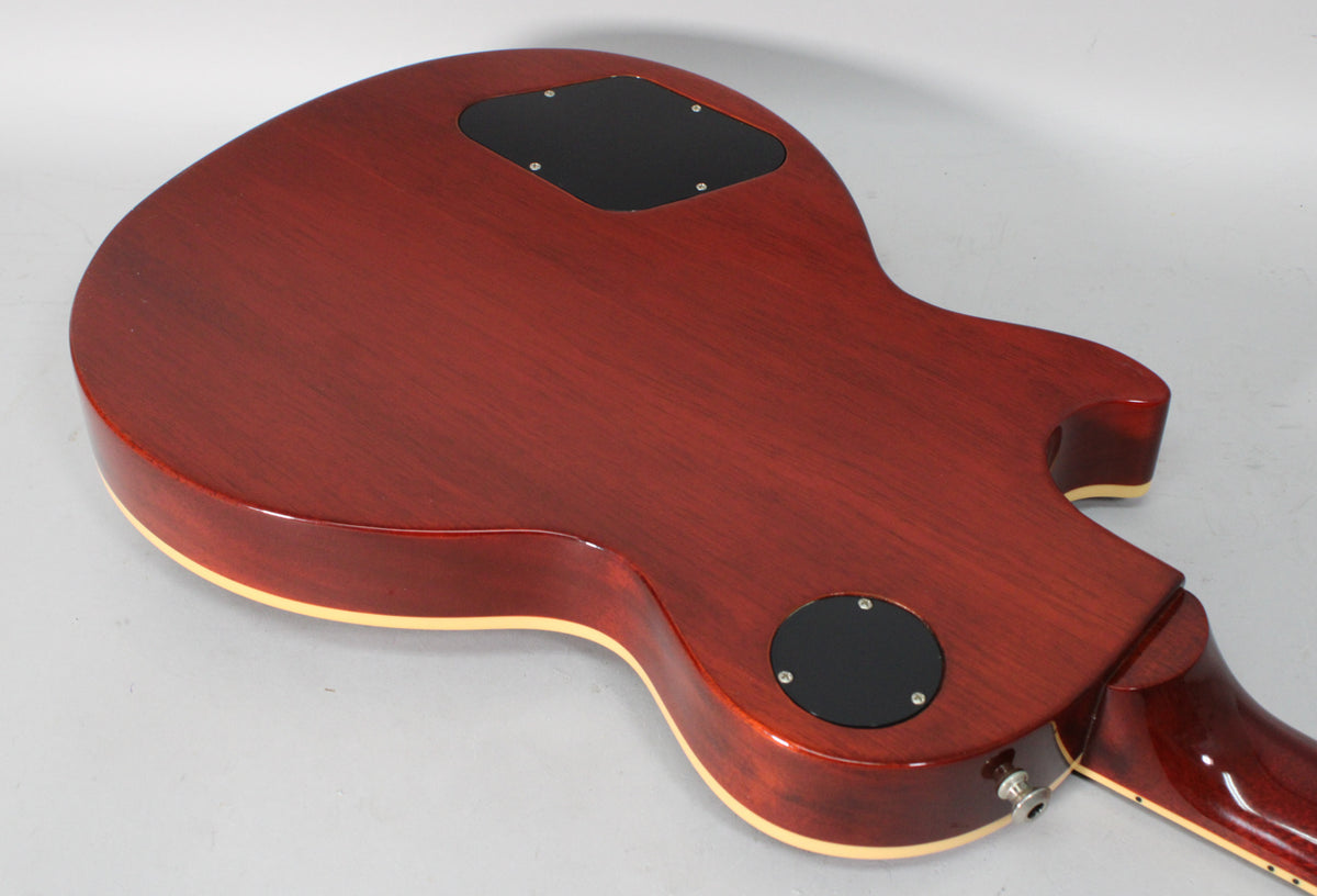 The back of a rootbeer-finished electric guitar, showing two black control cavity covers and the output jack.