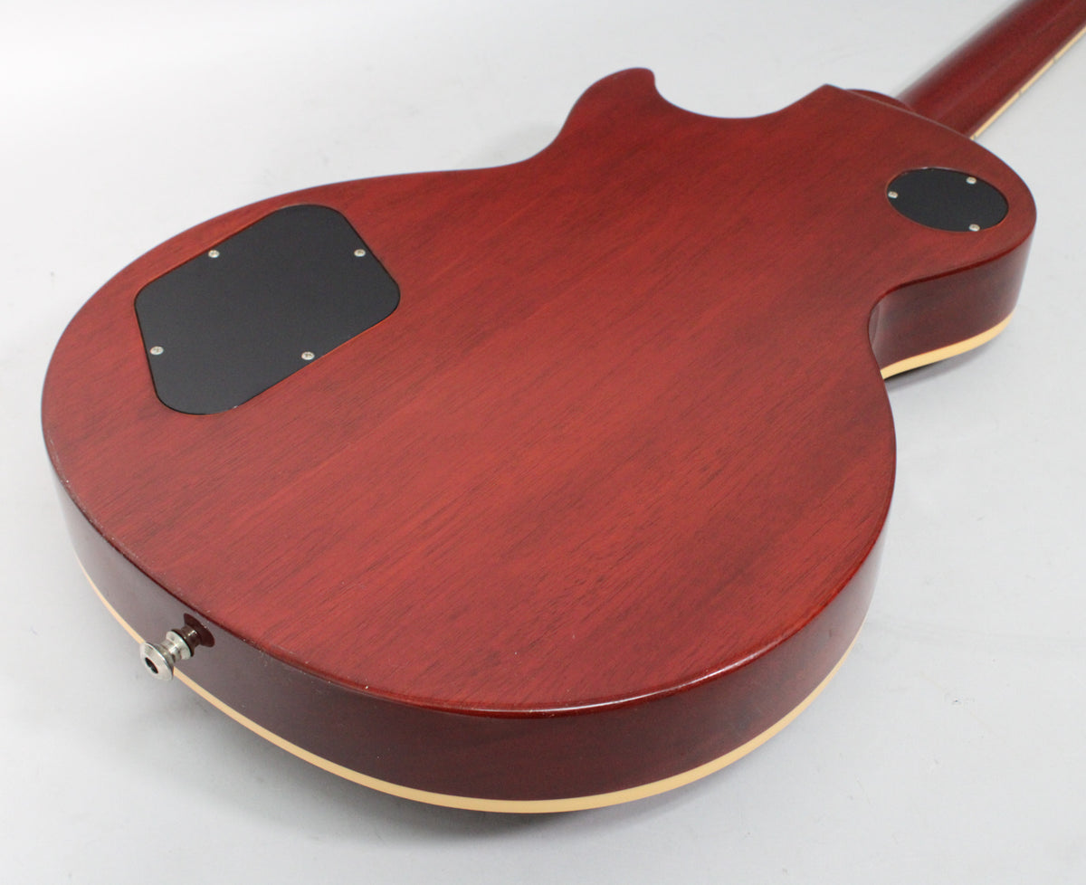 The guitar's rootbeer-stained mahogany back and neck are visible, with cream binding, two black control cavity covers, and a chrome output jack.