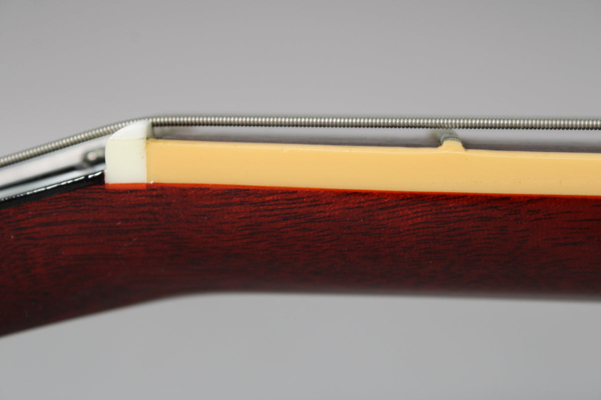 Close-up of the guitar's nut and first fret, showing the white nut, cream binding, and dark reddish-brown fretboard.