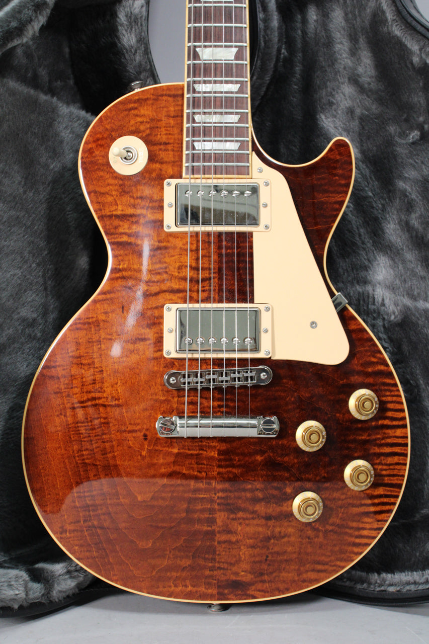 A close-up of a rootbeer burst Les Paul guitar, showing the body, pickups, bridge, controls, and part of the fretboard.