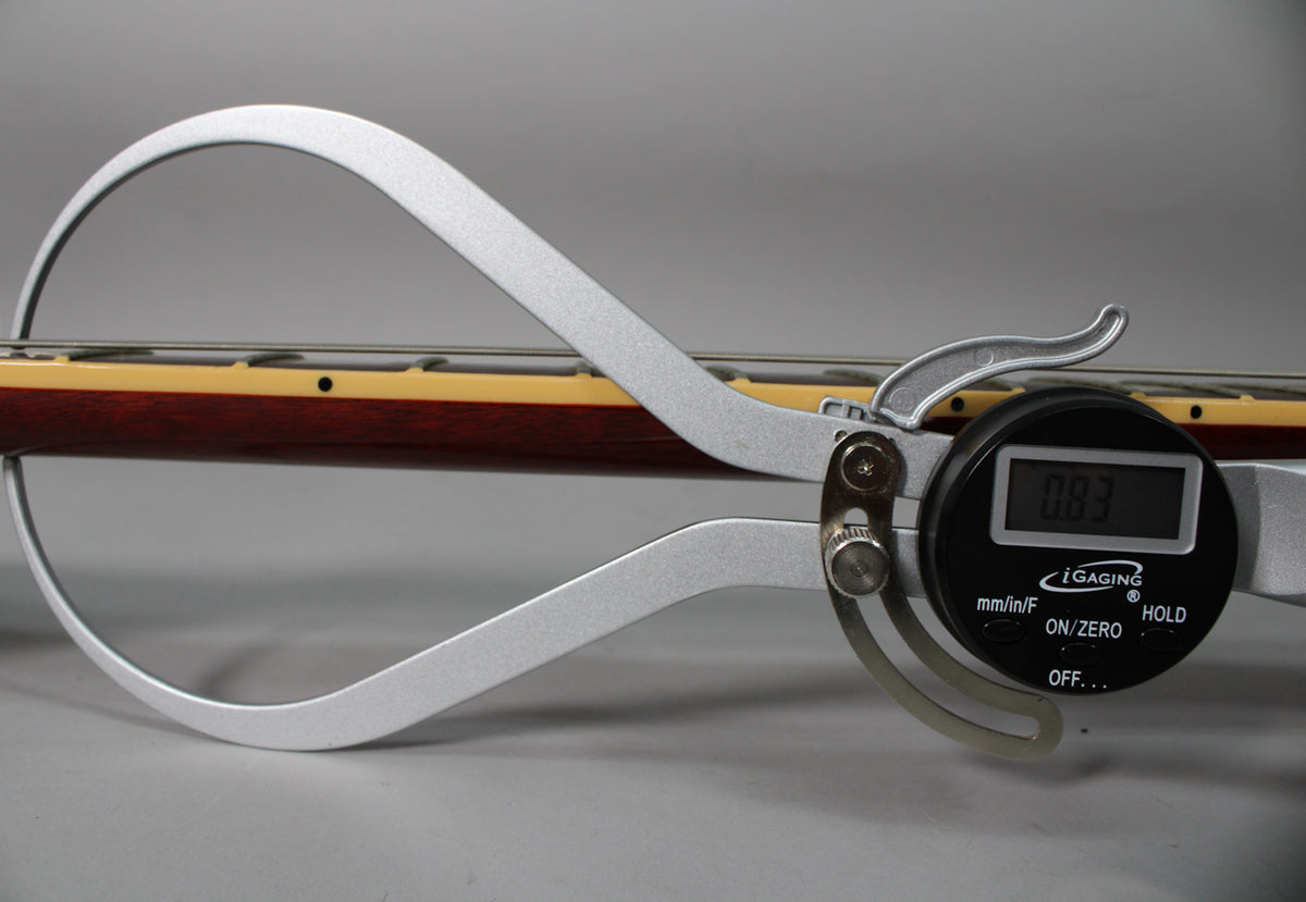 A digital caliper measures the neck thickness of the guitar, showing 0.83 inches, with a dark rosewood fretboard and cream binding.