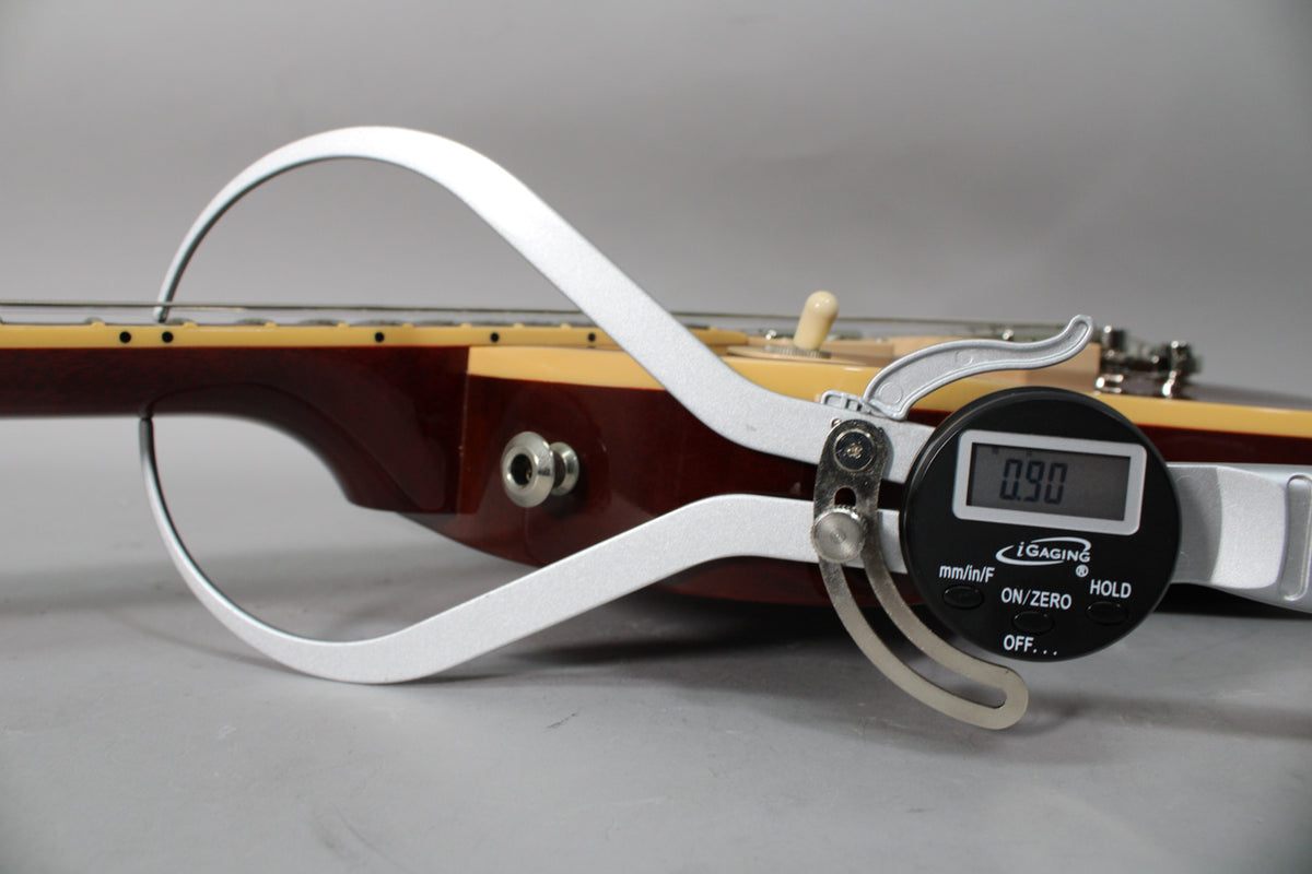 A digital caliper measures the string height at 0.90mm above the frets on the dark rootbeer body.