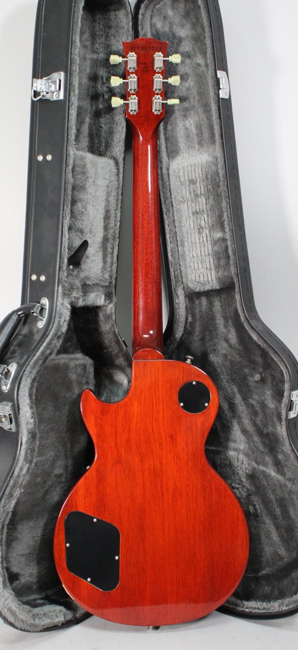 The guitar's rootbeer-stained back and neck are visible, with black control cavity covers and a black hard shell case with grey fur lining.