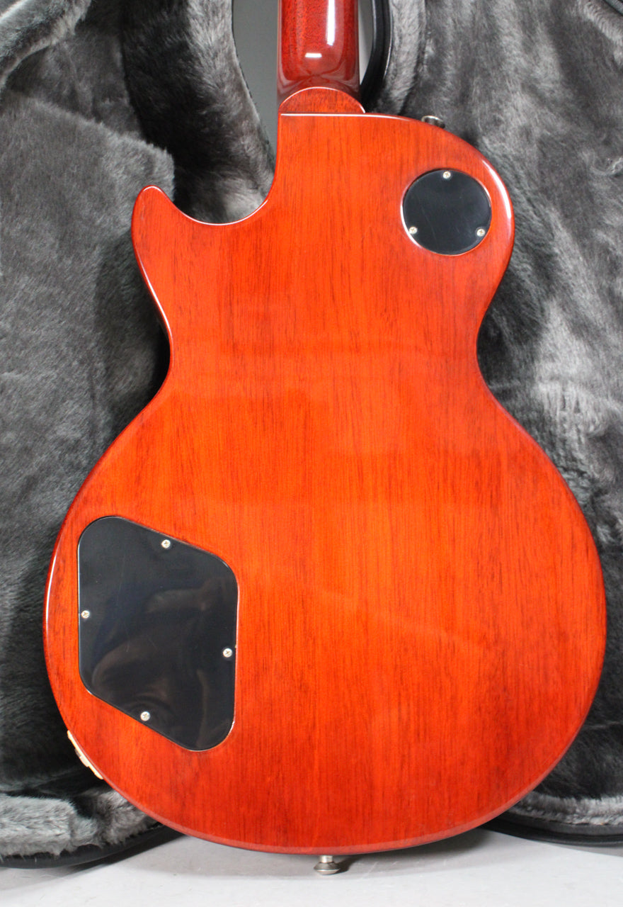 The back of a rootbeer-colored electric guitar with a glossy finish, showing two black control cavity covers and a strap button.