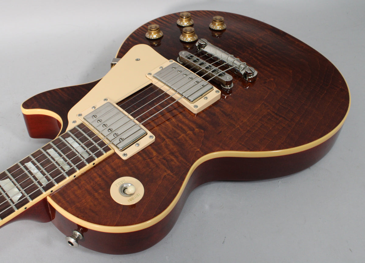 Upper body of a dark brown flamed top electric guitar, showing cream binding, pickups, and gold-capped control knobs.