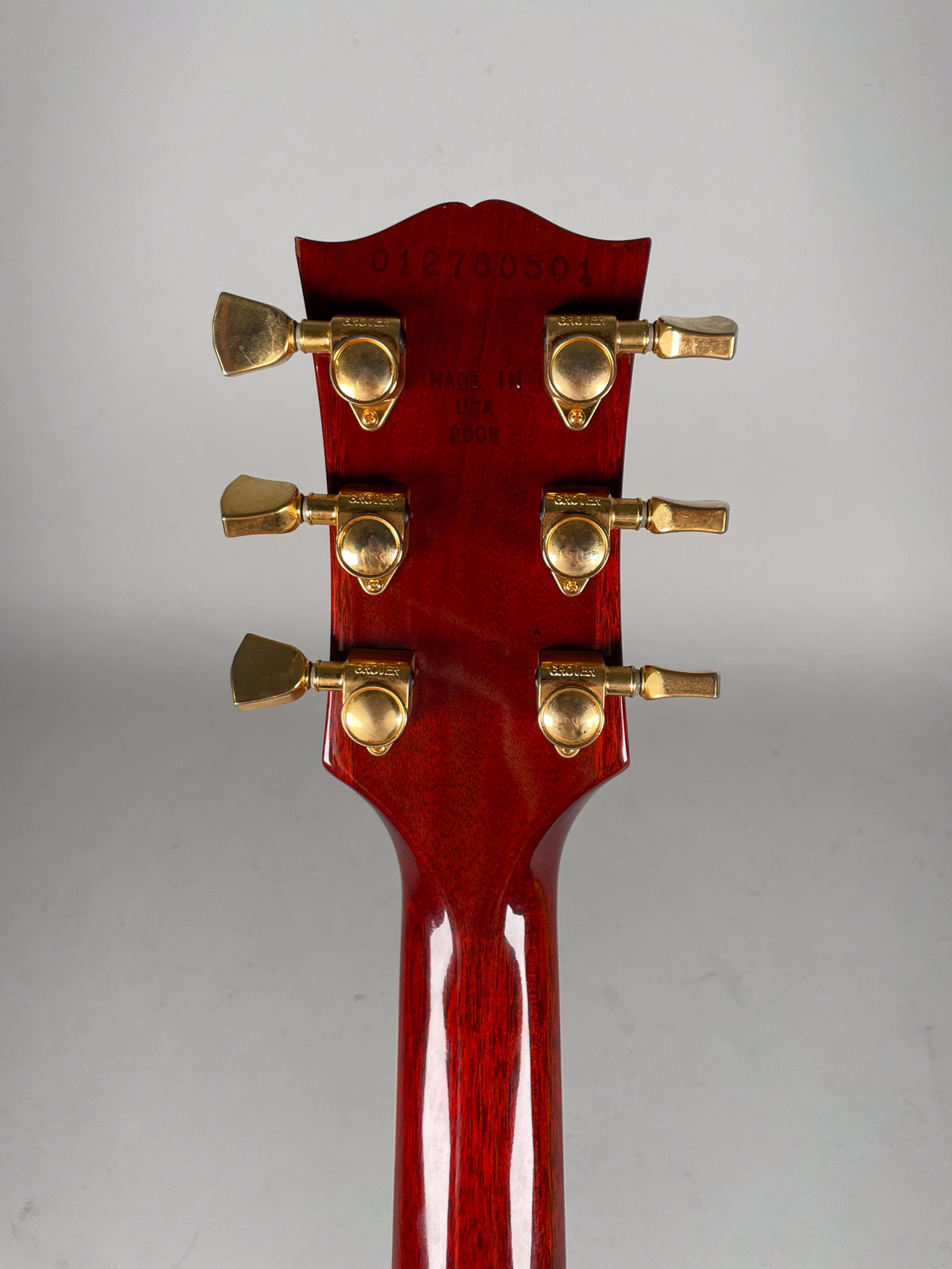 The back of a cherry sunburst headstock and neck, with six gold Grover tuners showing light wear.