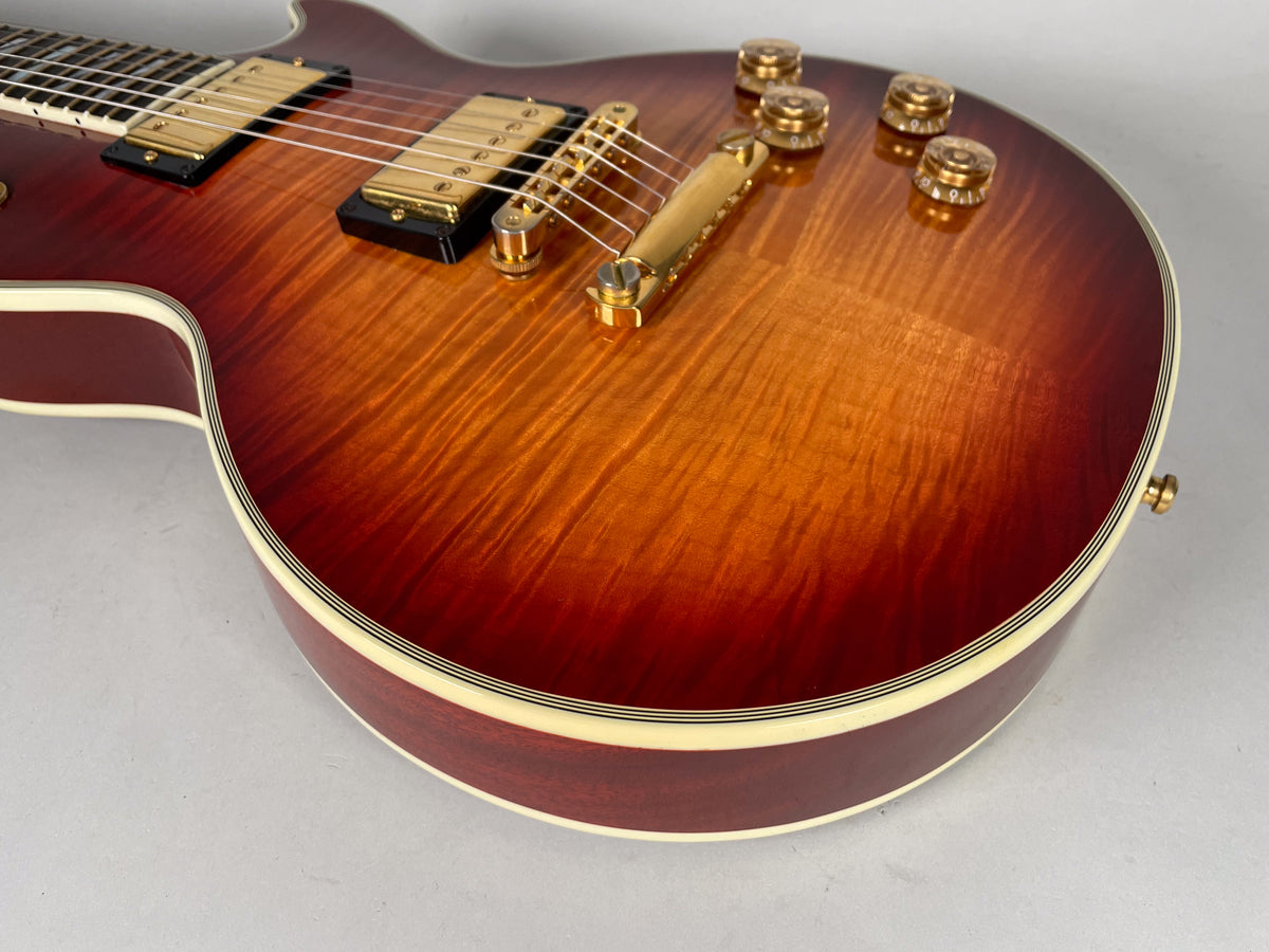 Close-up of the cherry sunburst Les Paul Supreme's flame maple top, showing gold hardware, cream binding, and four amber speed knobs.