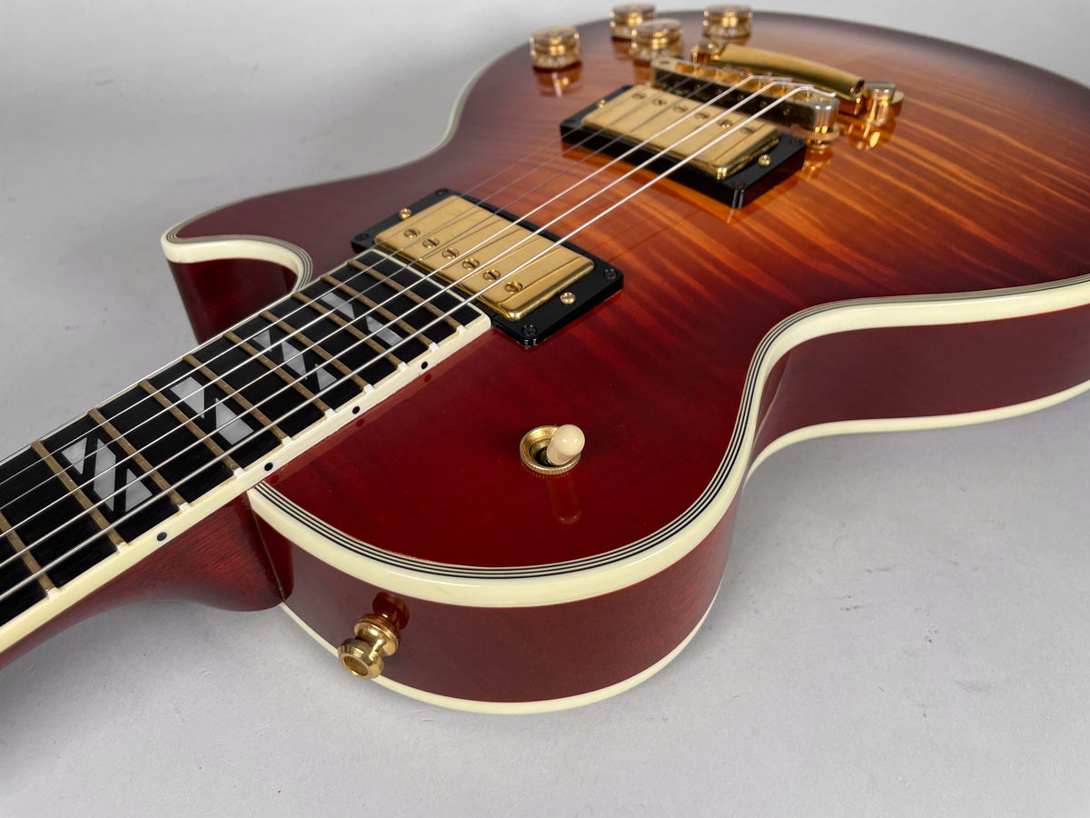 Cherry sunburst guitar body with gold hardware, cream binding, and trapezoid fretboard inlays, viewed from the lower bout.