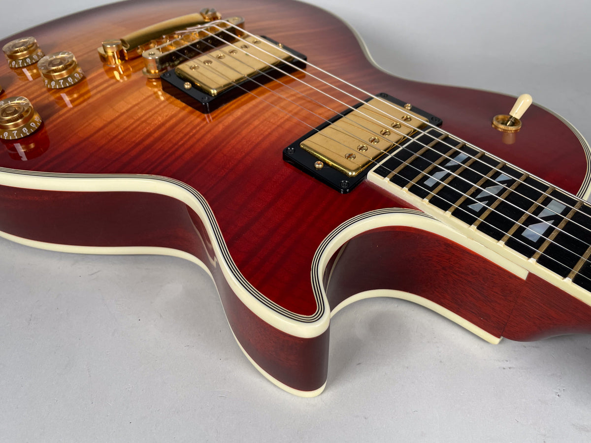Close-up of a cherry sunburst guitar with gold hardware, cream binding, and trapezoid fretboard inlays, viewed from the upper bout.