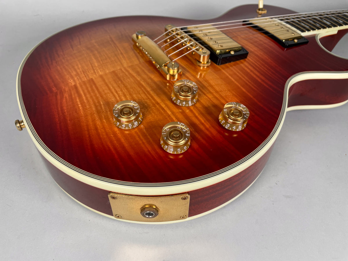 Close-up of the guitar's cherry sunburst flame maple top, showing four clear gold-numbered control knobs and gold hardware.