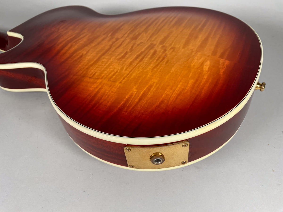 The guitar's cherry sunburst back shows flame maple grain, cream binding, and a gold output jack plate with some wear.