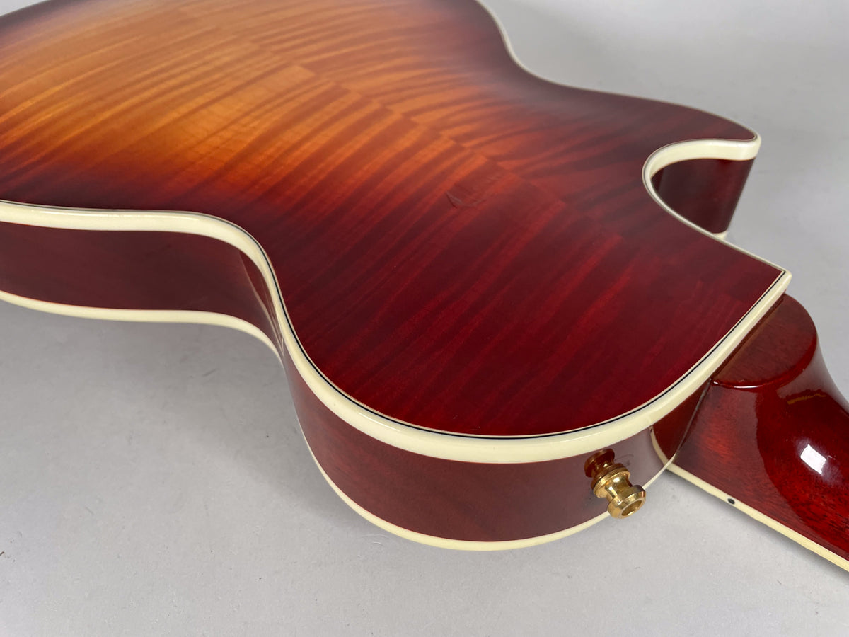 Close-up of the lower bout and cutaway of a cherry sunburst guitar, showing flame maple, cream binding, and a gold output jack.