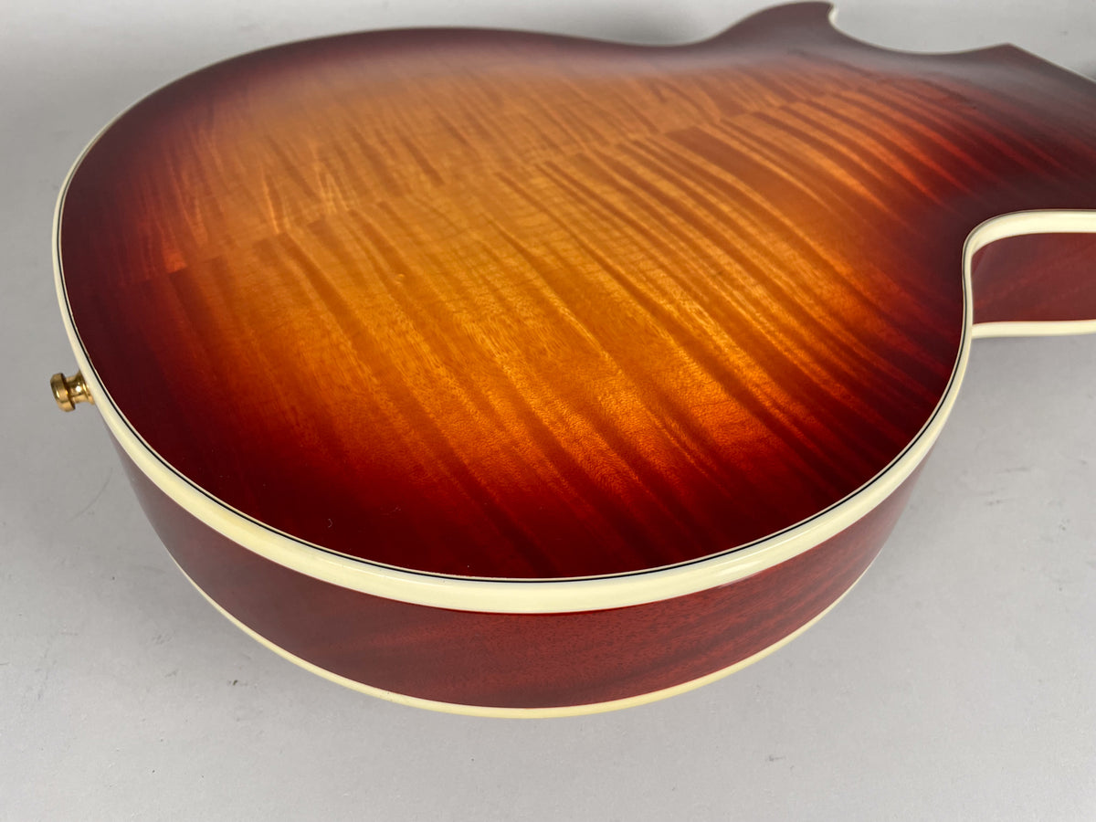 The guitar's cherry sunburst back, with prominent flame maple grain, shows a gold strap button and cream binding.
