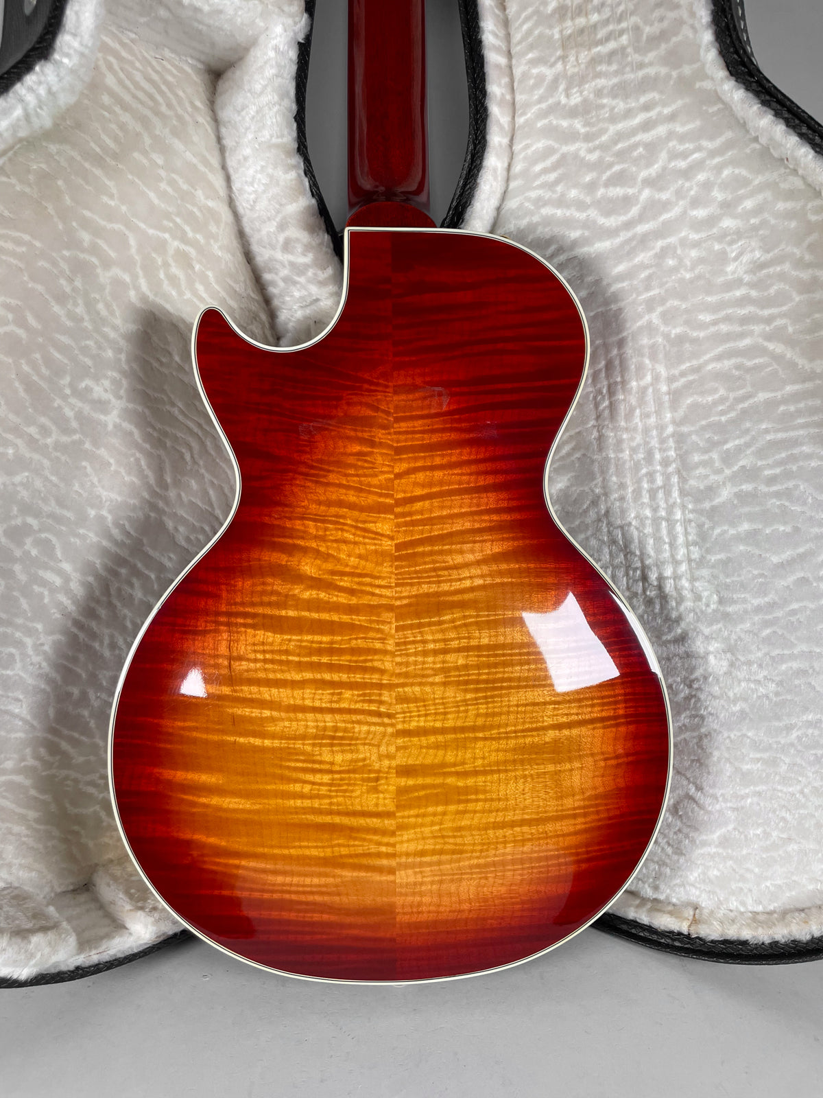 The guitar's cherry sunburst back shows flame maple grain, with a few light scratches, resting in a white plush-lined case.