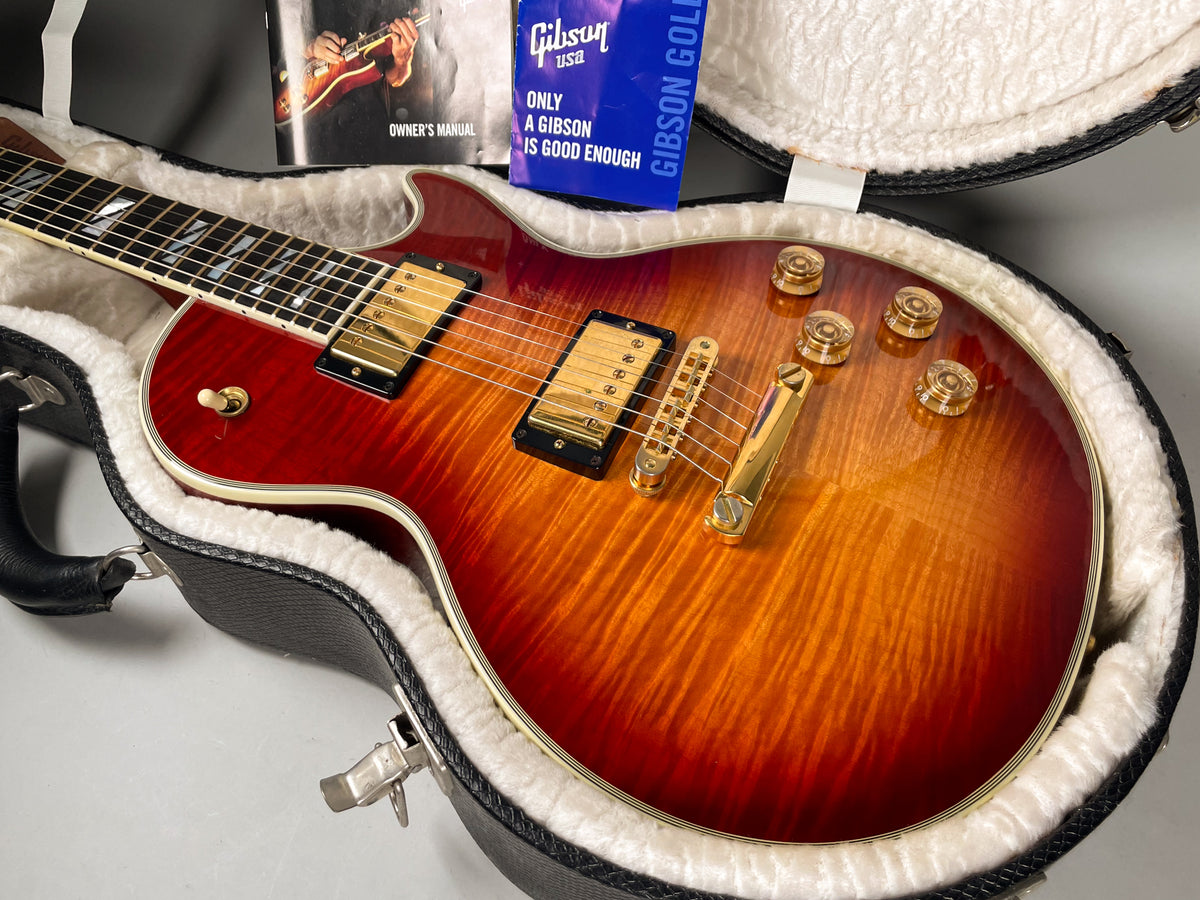 Cherry sunburst electric guitar with gold hardware, including four control knobs, in a black hard case with white plush lining.