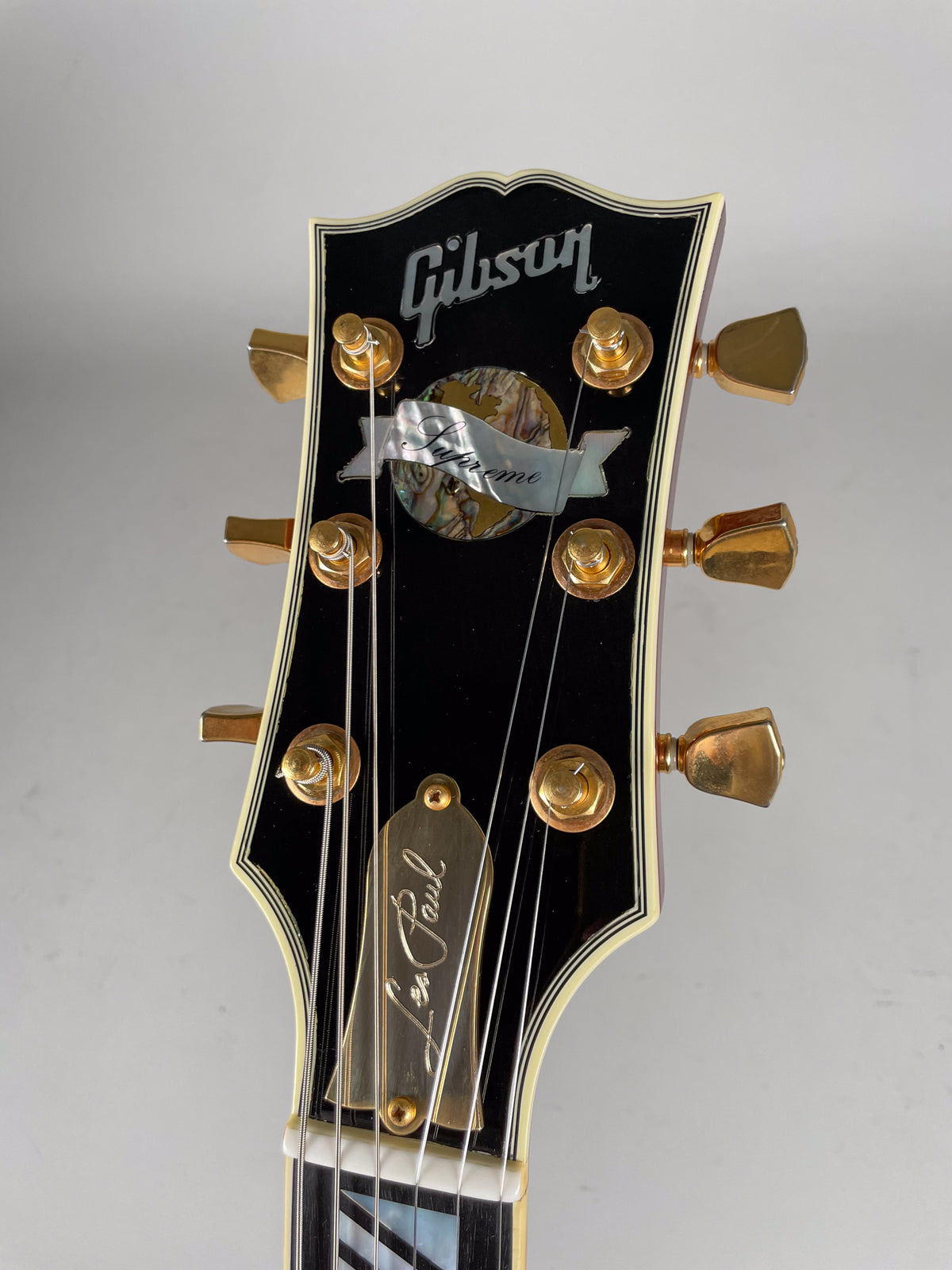 Close-up of the black headstock with gold tuners, mother-of-pearl inlay, and a gold truss rod cover, showing light wear.