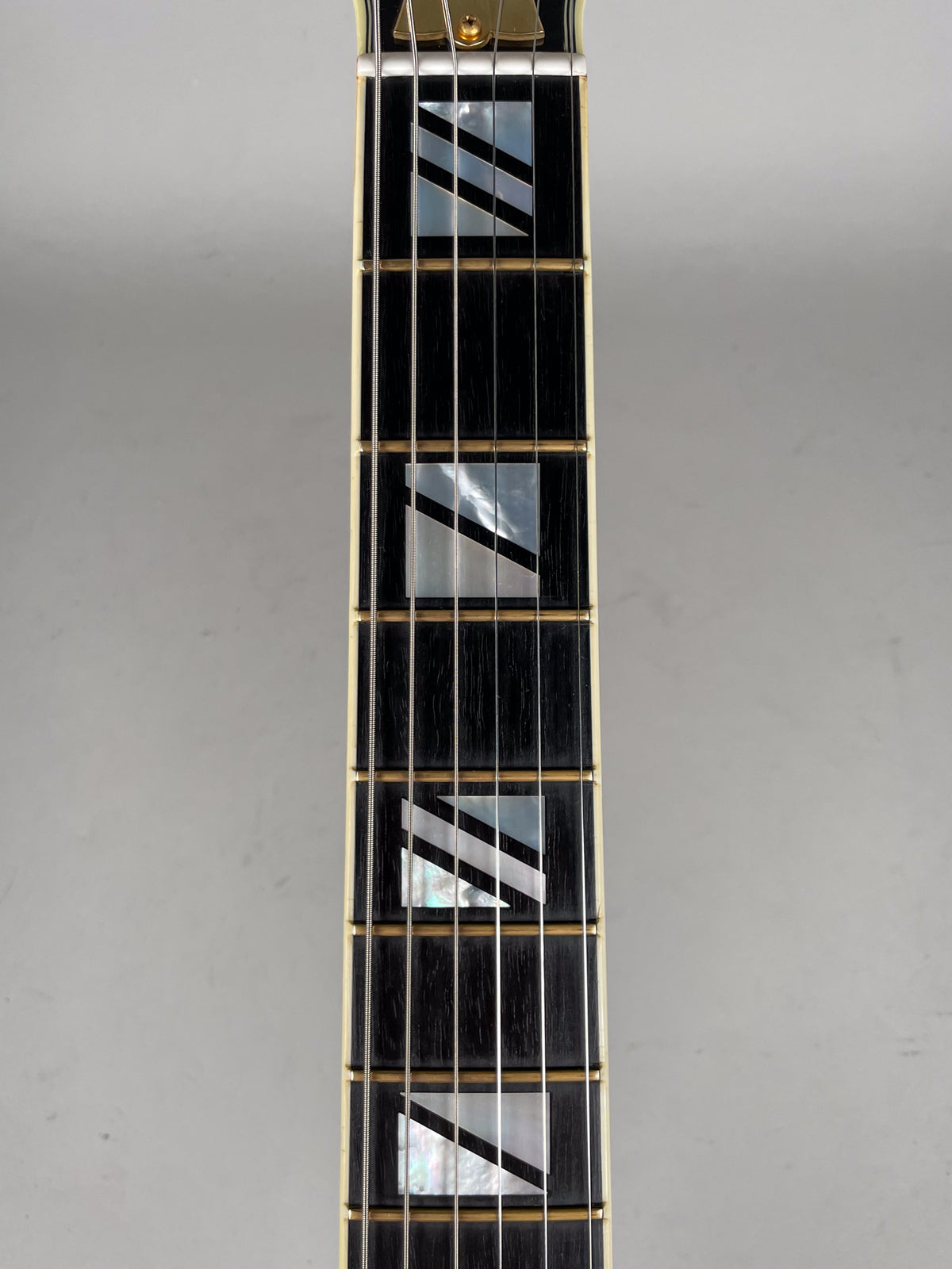 The ebony fretboard with mother-of-pearl split-block inlays and gold frets is framed from the nut down to the 7th fret.
