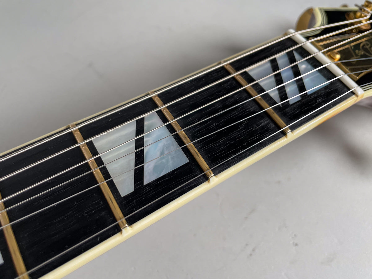 Close-up of the guitar's dark fretboard with mother-of-pearl block inlays, gold frets, and cream binding.