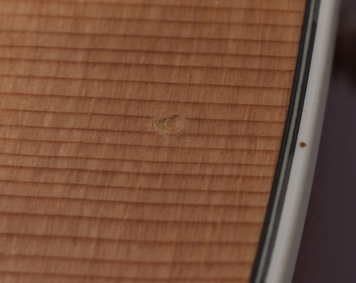 Close-up of the natural wood grain top with a small knot and a dark speck on the white binding.