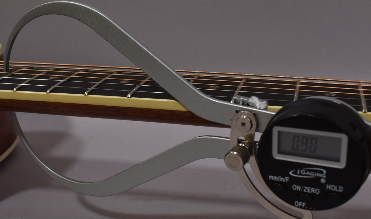 A digital caliper measures the string height at the 12th fret, showing 0.90 on its display.