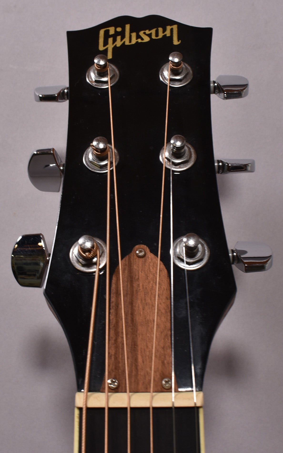 A close-up of the guitar's glossy black headstock, showing six chrome tuners, a dark wood truss rod cover, and light strings.