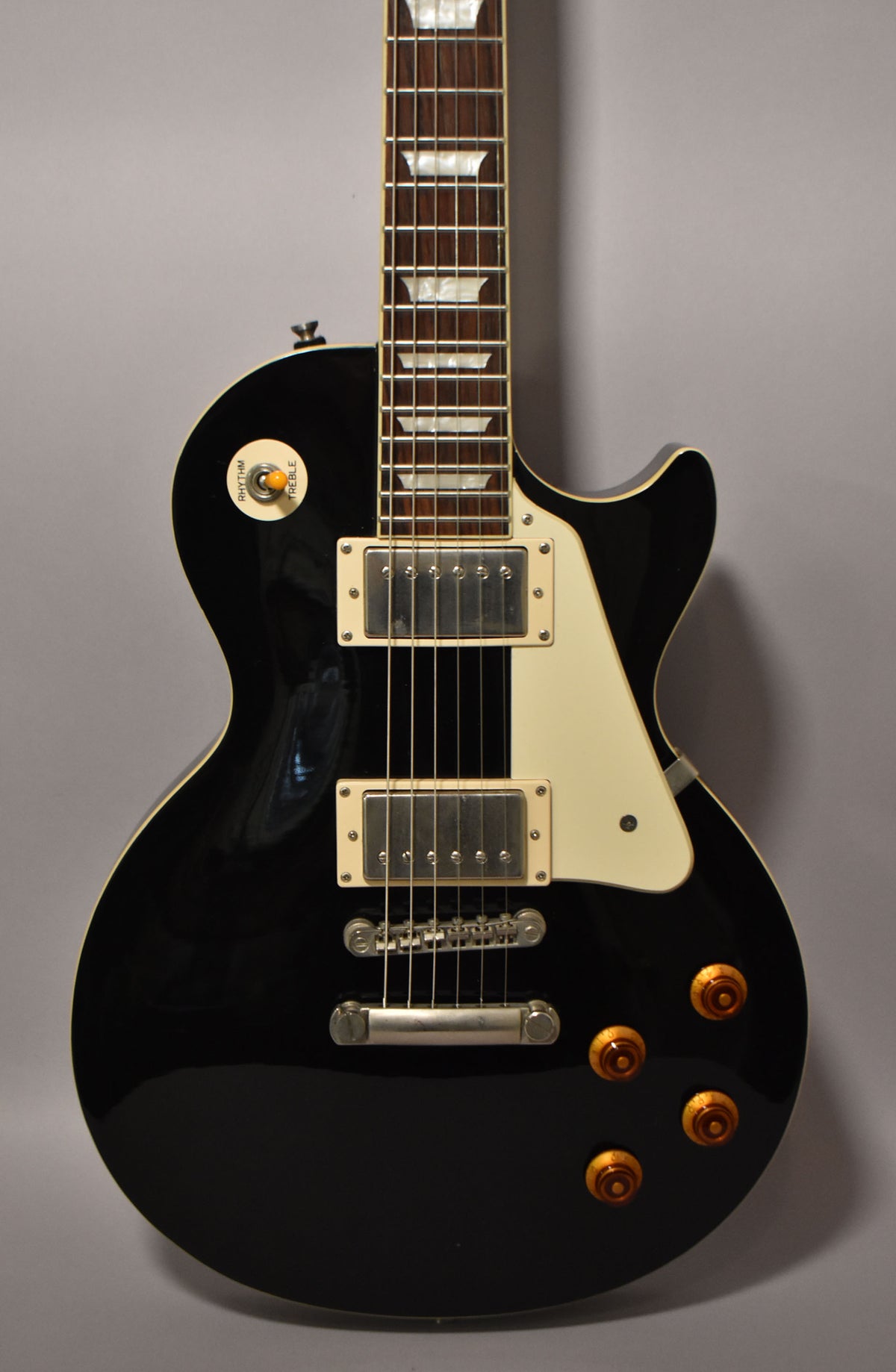 A black Epiphone Les Paul Standard guitar with a cream pickguard, two humbucker pickups, and four amber control knobs.