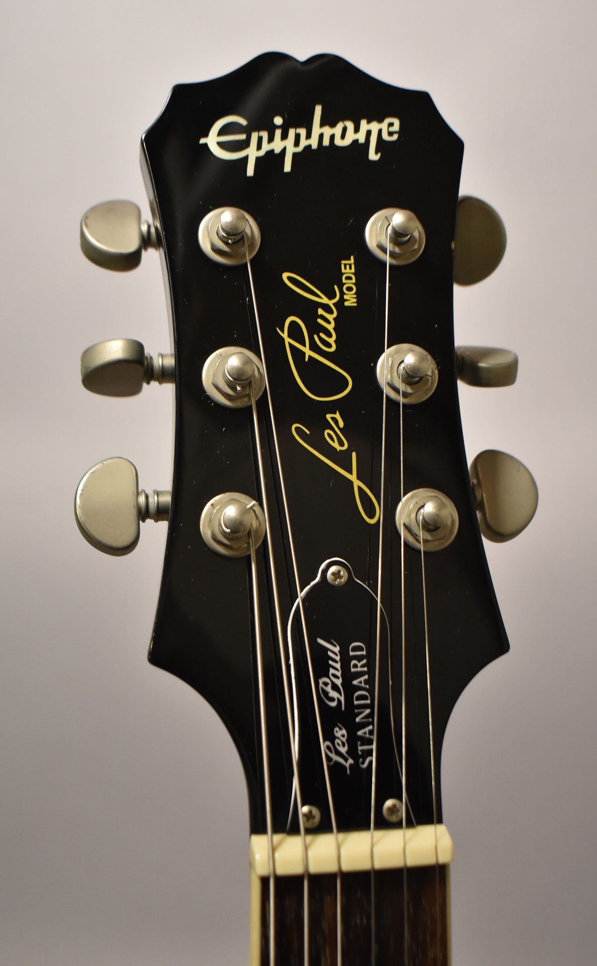 Close-up of the ebony headstock with a glossy finish, showing six chrome tuners, a cream nut, and light string wear.