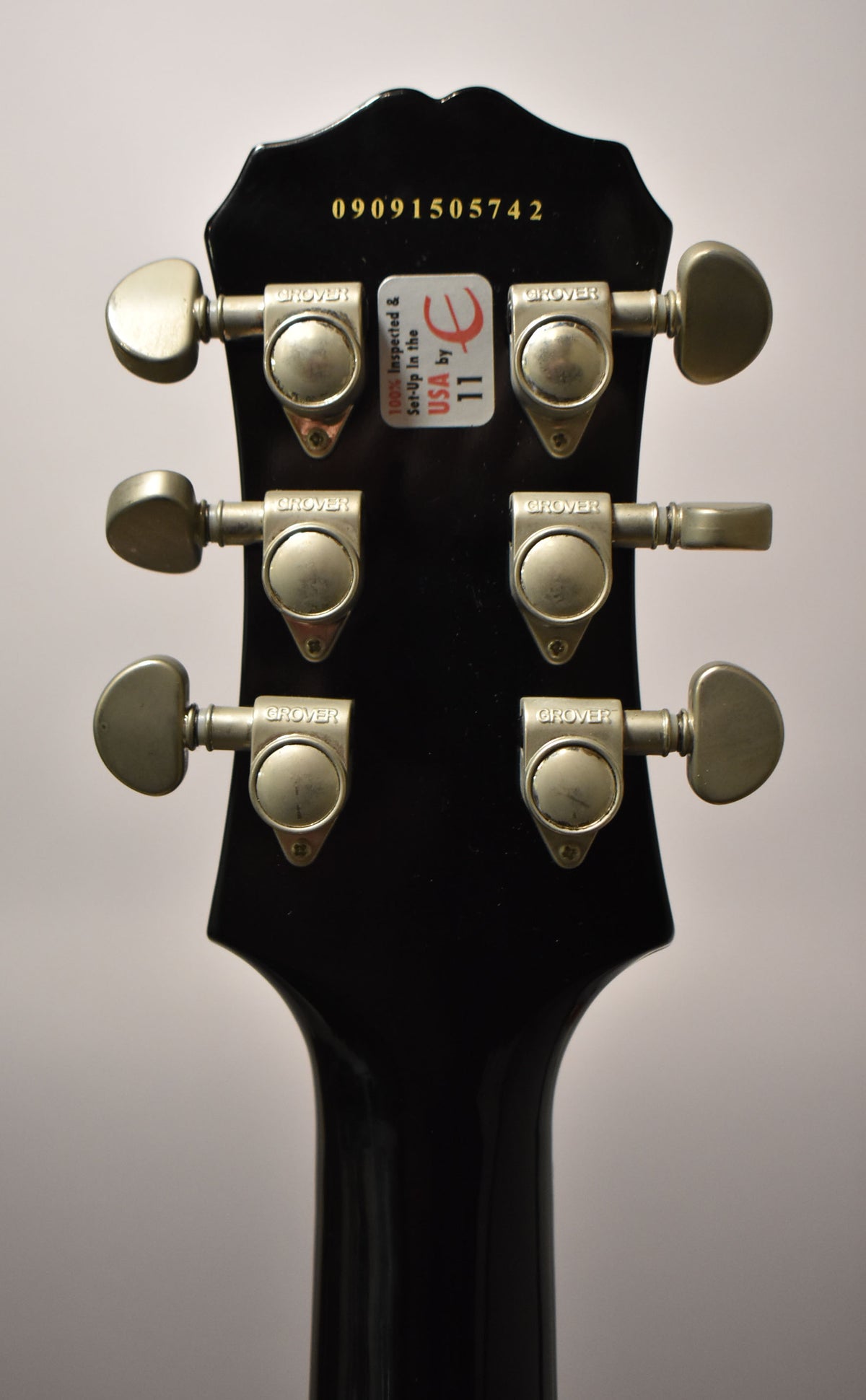 Rear view of the black gloss headstock and neck, showing six Grover tuners with tarnished buttons and a serial number.