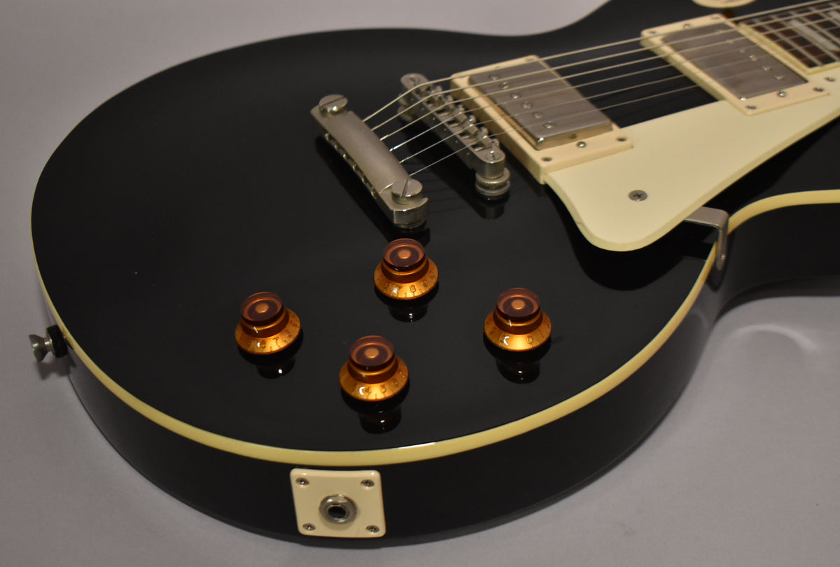 Upper body of a black guitar with cream binding, four amber top hat knobs, nickel hardware, and a cream pickguard.