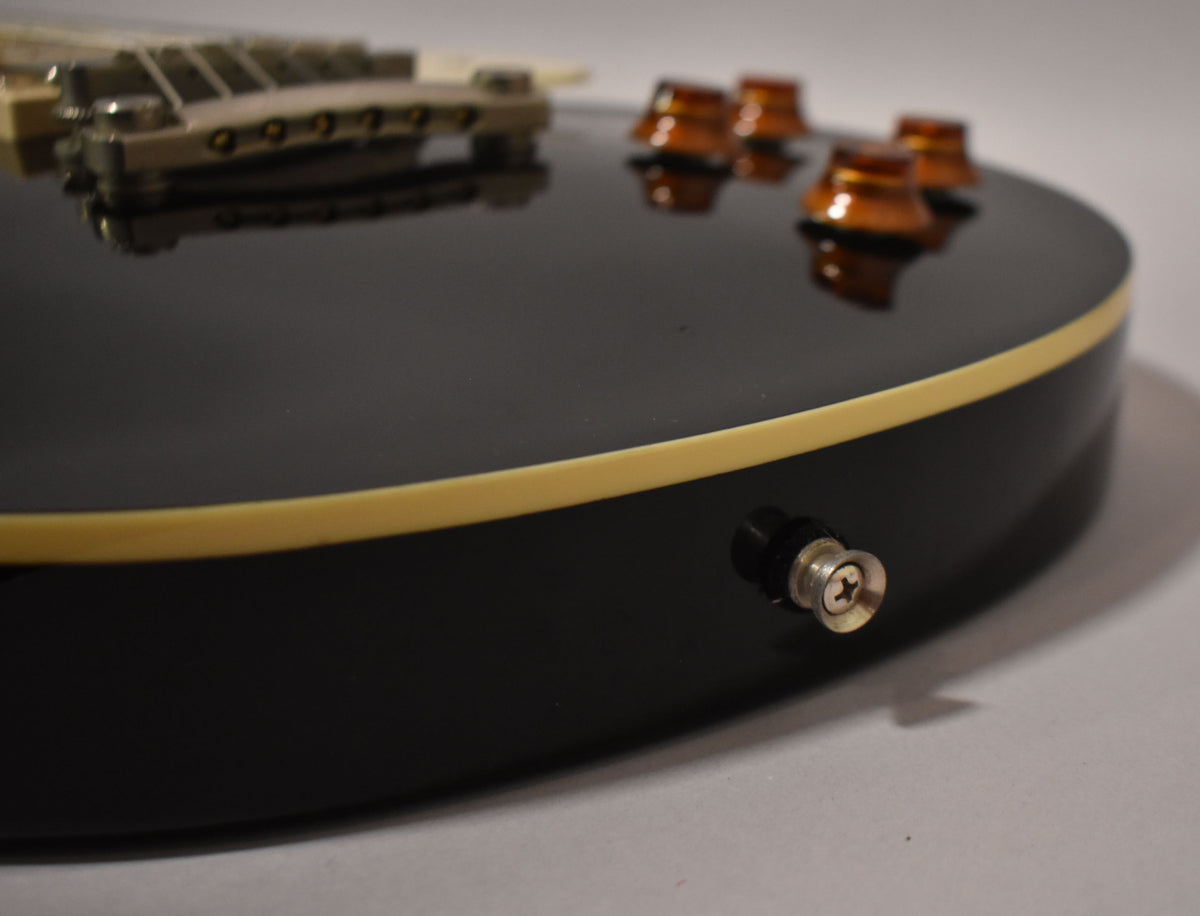 Close-up of the guitar's lower bout, showing the glossy black finish, cream binding, output jack, and four amber control knobs.