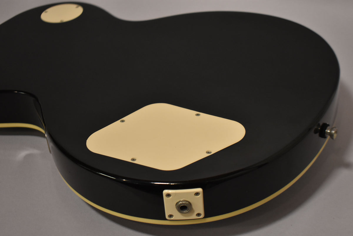 The guitar's glossy black back, with cream binding and control cavity covers, shows light wear and a chrome strap button.