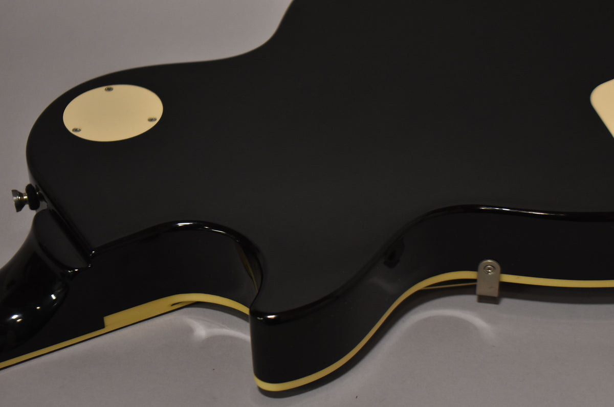 The glossy black guitar body, with cream binding, is angled to show the back and side, revealing a cream control cavity cover.