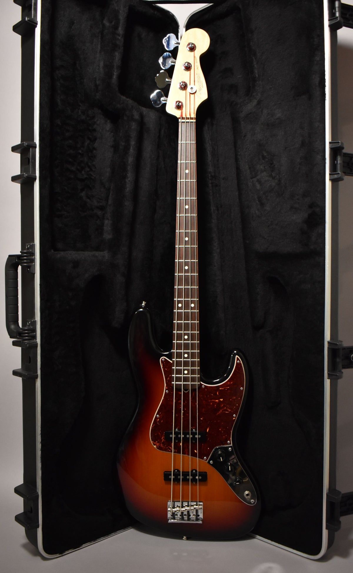 Full-length shot of a sunburst bass with a tortoiseshell pickguard, resting upright in a black hard case.