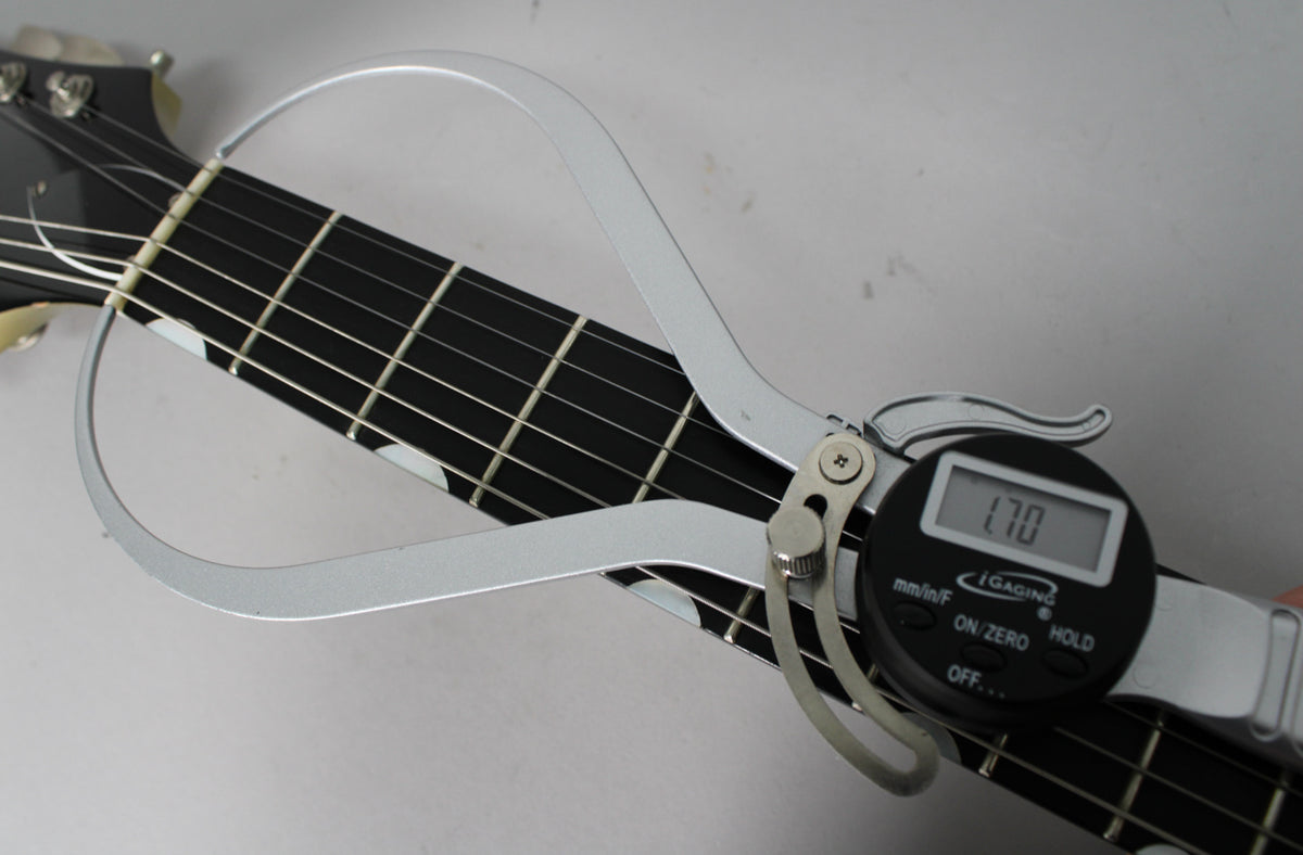 Close-up of the guitar's black fretboard with white block inlays, showing a digital caliper measuring the nut width at 1.70.