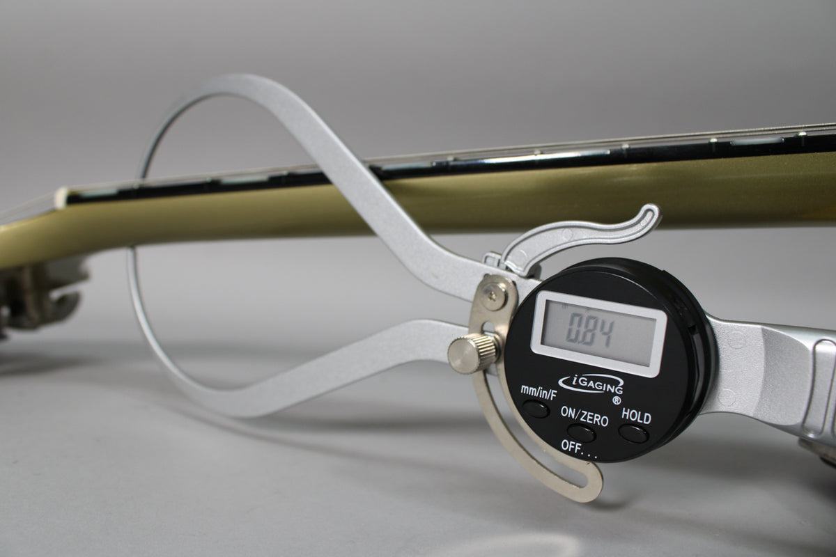 A digital caliper measures the guitar's neck relief, showing 0.84mm, with the tan neck and dark fretboard visible.