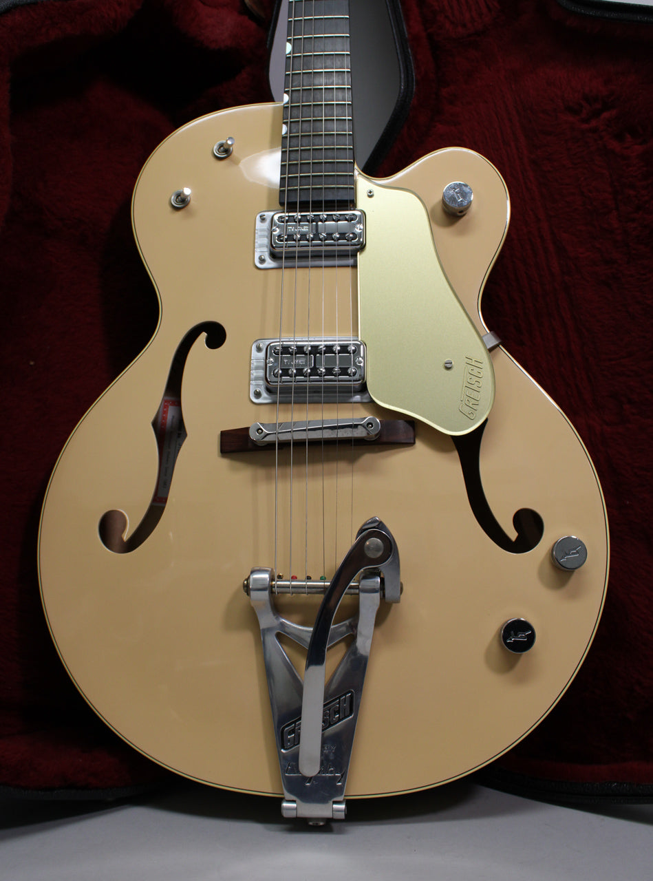Full-frame view of a tan hollow-body electric guitar with f-holes, a gold pickguard, chrome hardware, and a Bigsby vibrato.