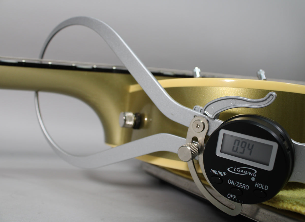 A digital caliper measures the neck thickness of the tan guitar, showing 0.94 inches at the 1st fret.