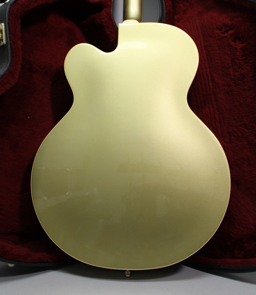 The full back of a gold metallic hollow-body electric guitar, showing light scratches and a strap button at the bottom.