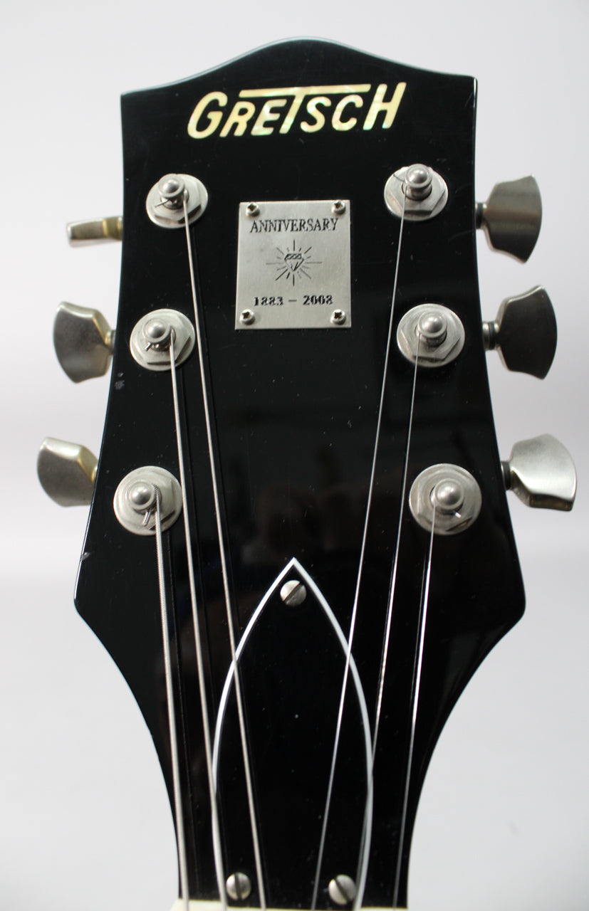 Close-up of the glossy black headstock with six silver tuners, a silver anniversary plaque, and a white truss rod cover.