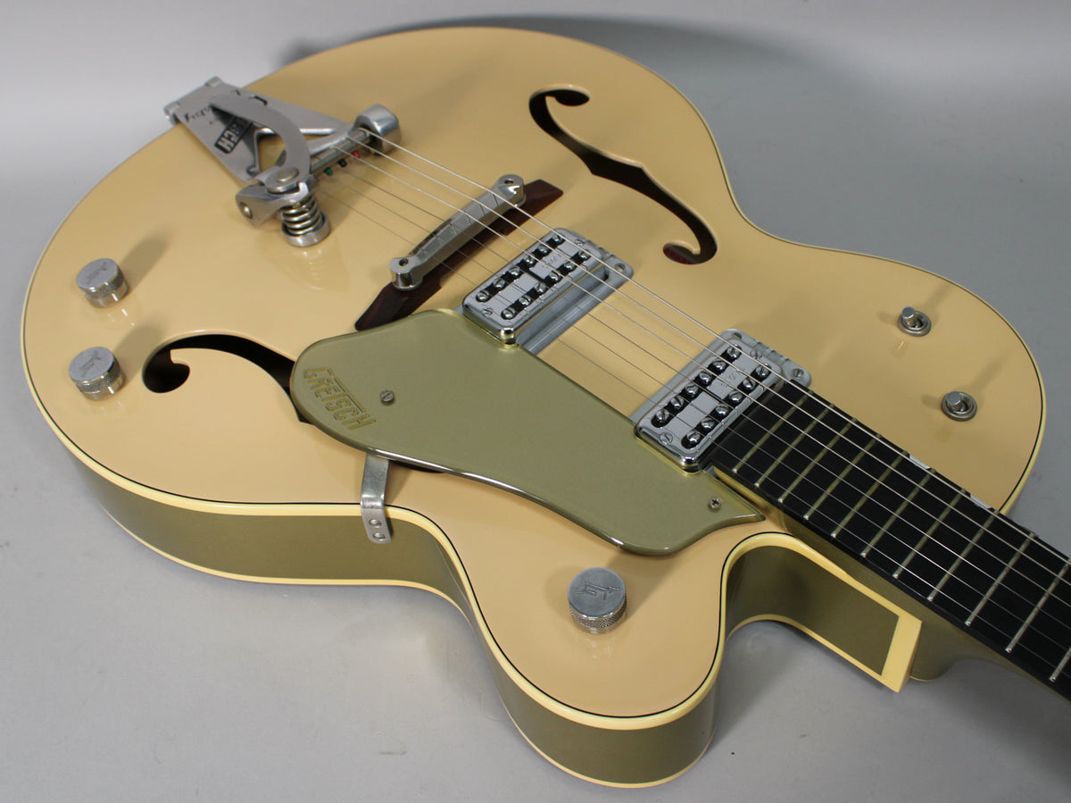 Tan hollow-body electric guitar, angled from above, showing the Bigsby vibrato, two humbuckers, and gold pickguard.